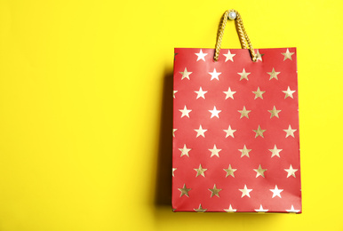 Photo of Red shopping paper bag with star pattern on yellow background, space for text