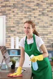 Photo of Young woman in apron and gloves cleaning office