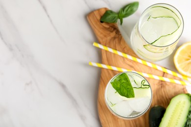 Tasty fresh cucumber water, sliced lemon and basil on white marble table, flat lay. Space for text