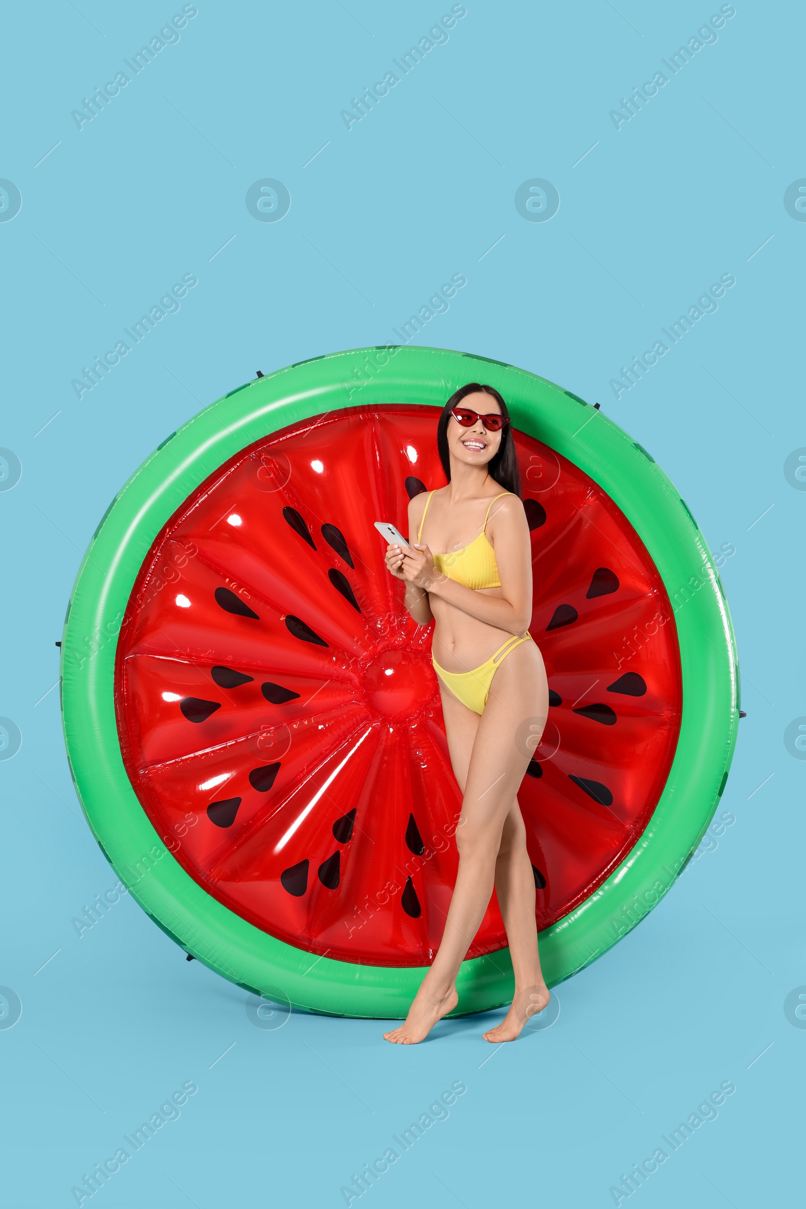 Photo of Young woman with smartphone near inflatable mattress against light blue background