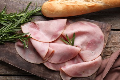 Slices of delicious ham, rosemary and baguette on wooden table, flat lay