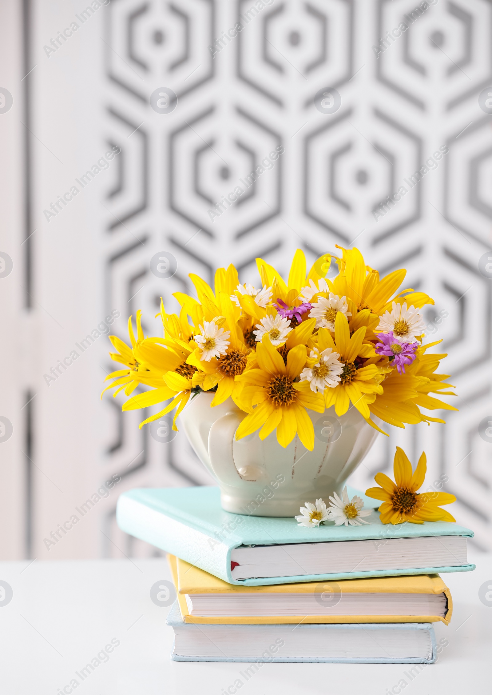 Photo of Beautiful bright flowers in cup and books on white table indoors