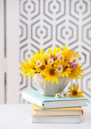 Beautiful bright flowers in cup and books on white table indoors