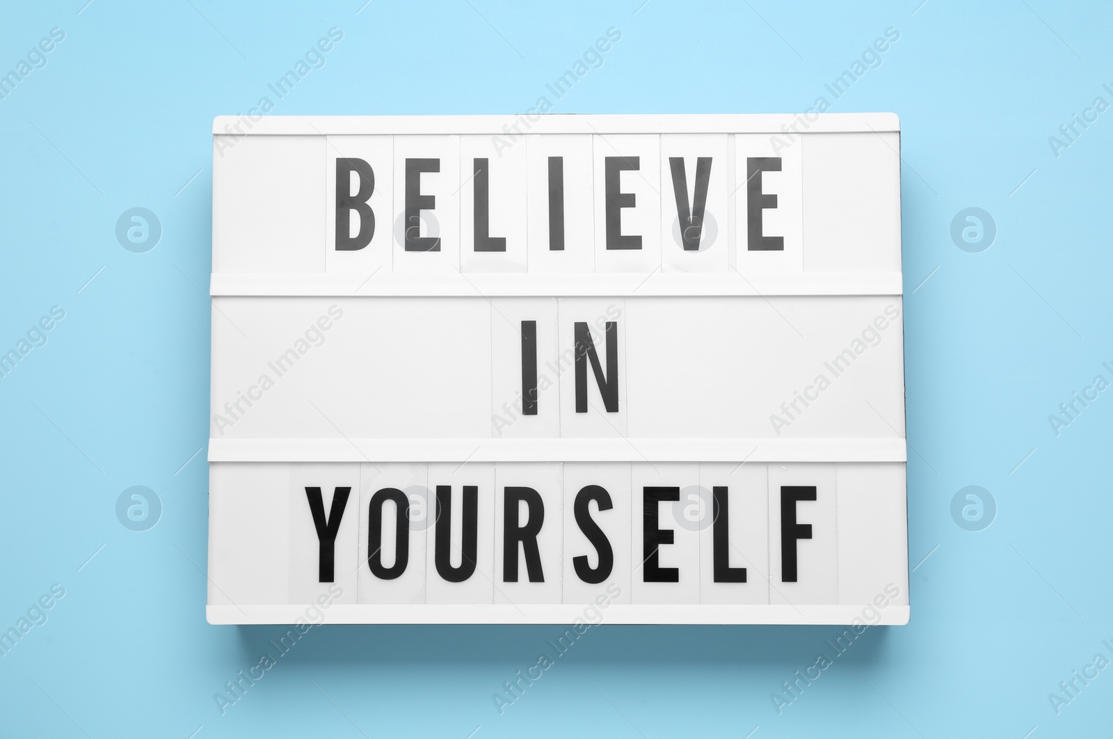 Photo of Lightbox with motivational quote Believe in Yourself on light blue background, top view