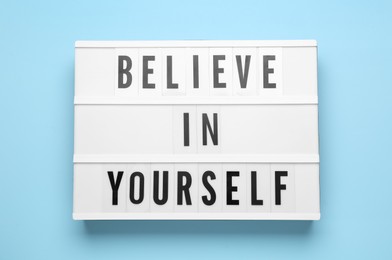Photo of Lightbox with motivational quote Believe in Yourself on light blue background, top view