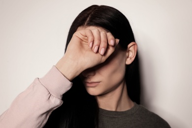 Young woman covering face against light background