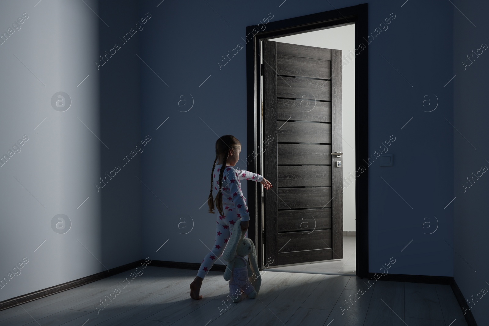 Photo of Girl in pajamas with toy bunny sleepwalking indoors at night