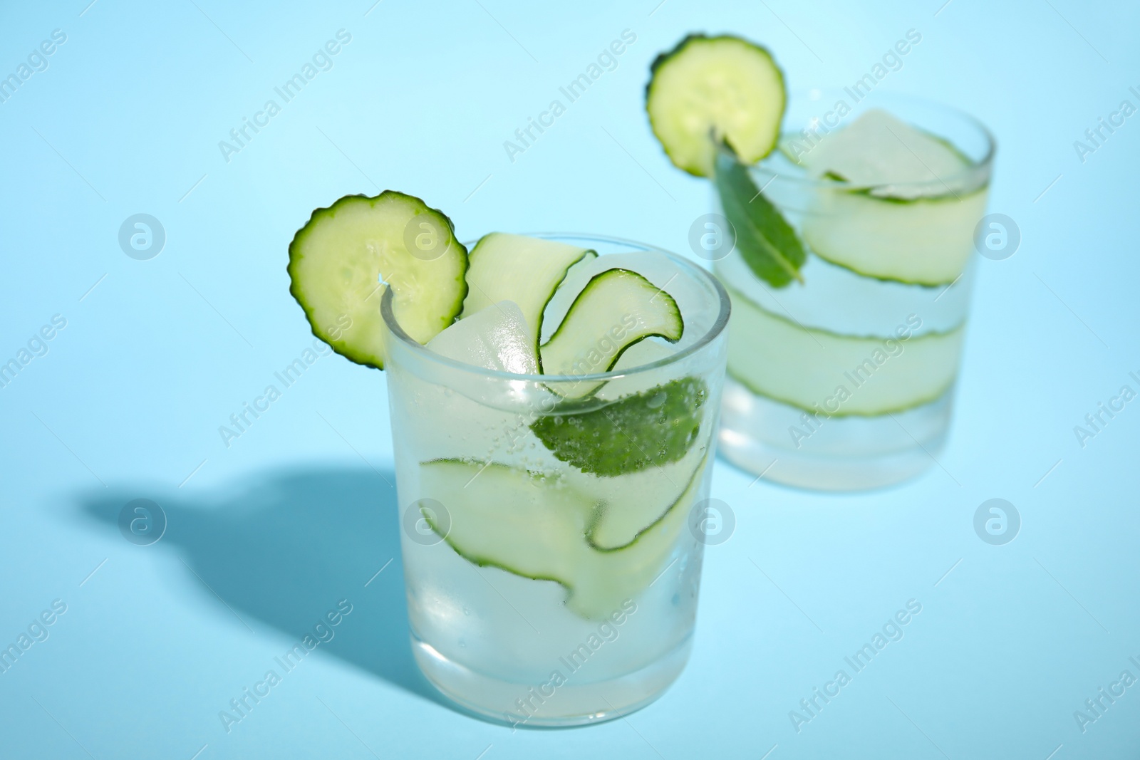 Photo of Tasty fresh cucumber water with mint on light blue background
