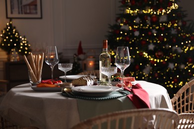 Photo of Christmas table setting with bottle of wine, appetizers and dishware indoors