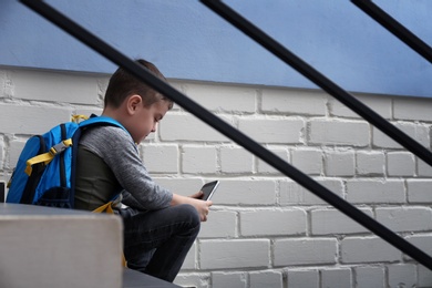 Photo of Sad little boy with mobile phone sitting on stairs indoors