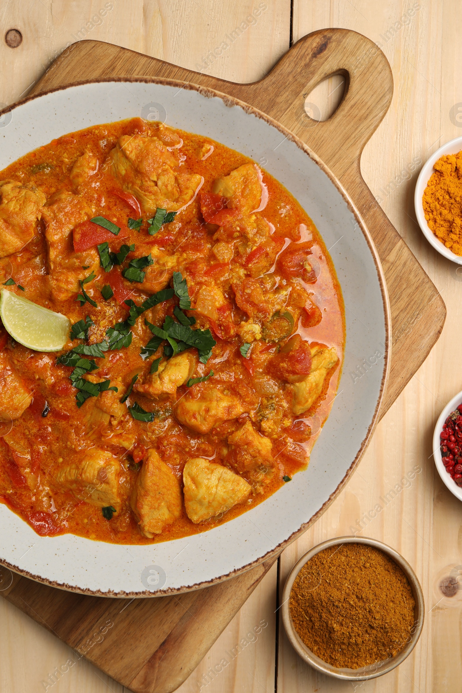 Photo of Delicious chicken curry and spices on wooden table, flat lay