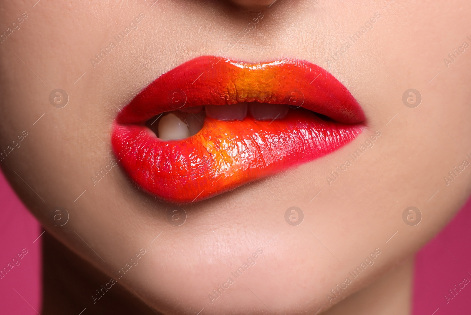 Photo of Young woman with beautiful makeup biting lip on pink background, closeup