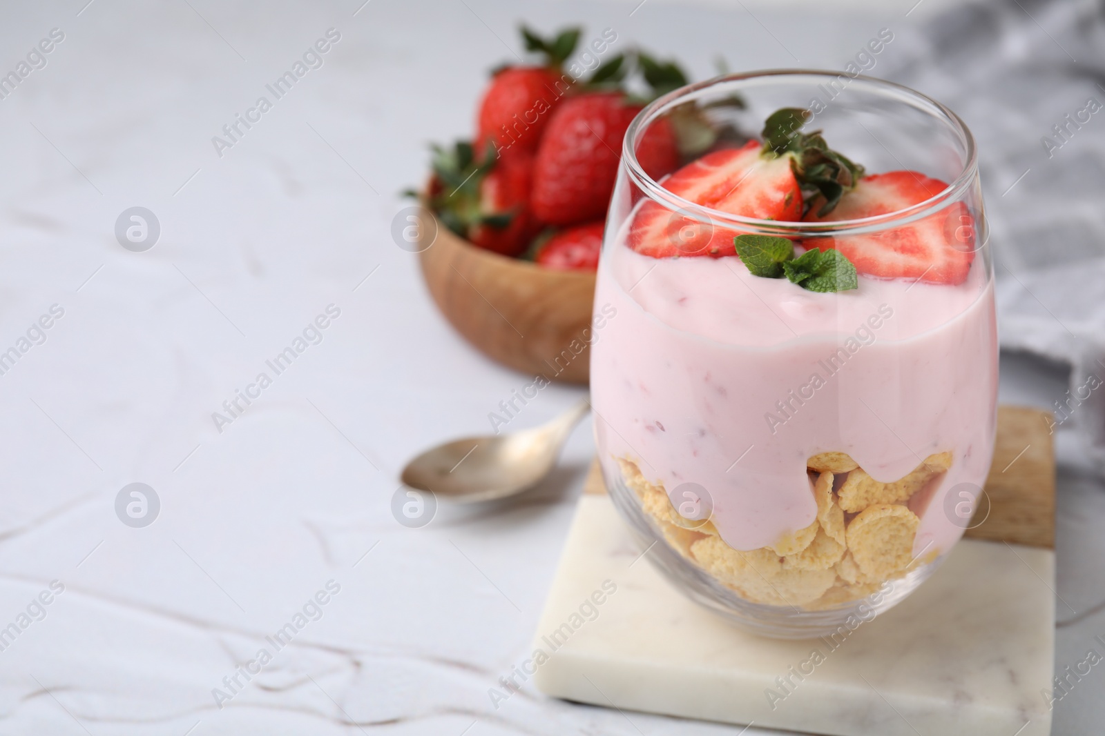 Photo of Glass with yogurt, strawberries and corn flakes on white textured table, closeup. Space for text