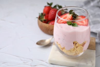 Glass with yogurt, strawberries and corn flakes on white textured table, closeup. Space for text