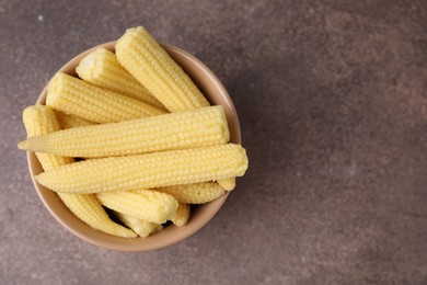 Photo of Tasty fresh yellow baby corns in bowl on brown table, top view. Space for text