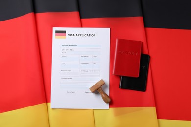 Immigration to Germany. Visa application form, passports and stamp on flag, flat lay