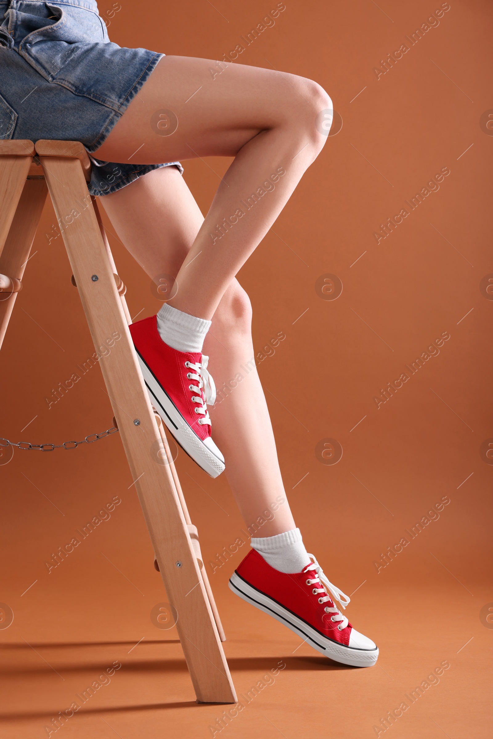 Photo of Woman in red classic old school sneakers on ladder against brown background, closeup