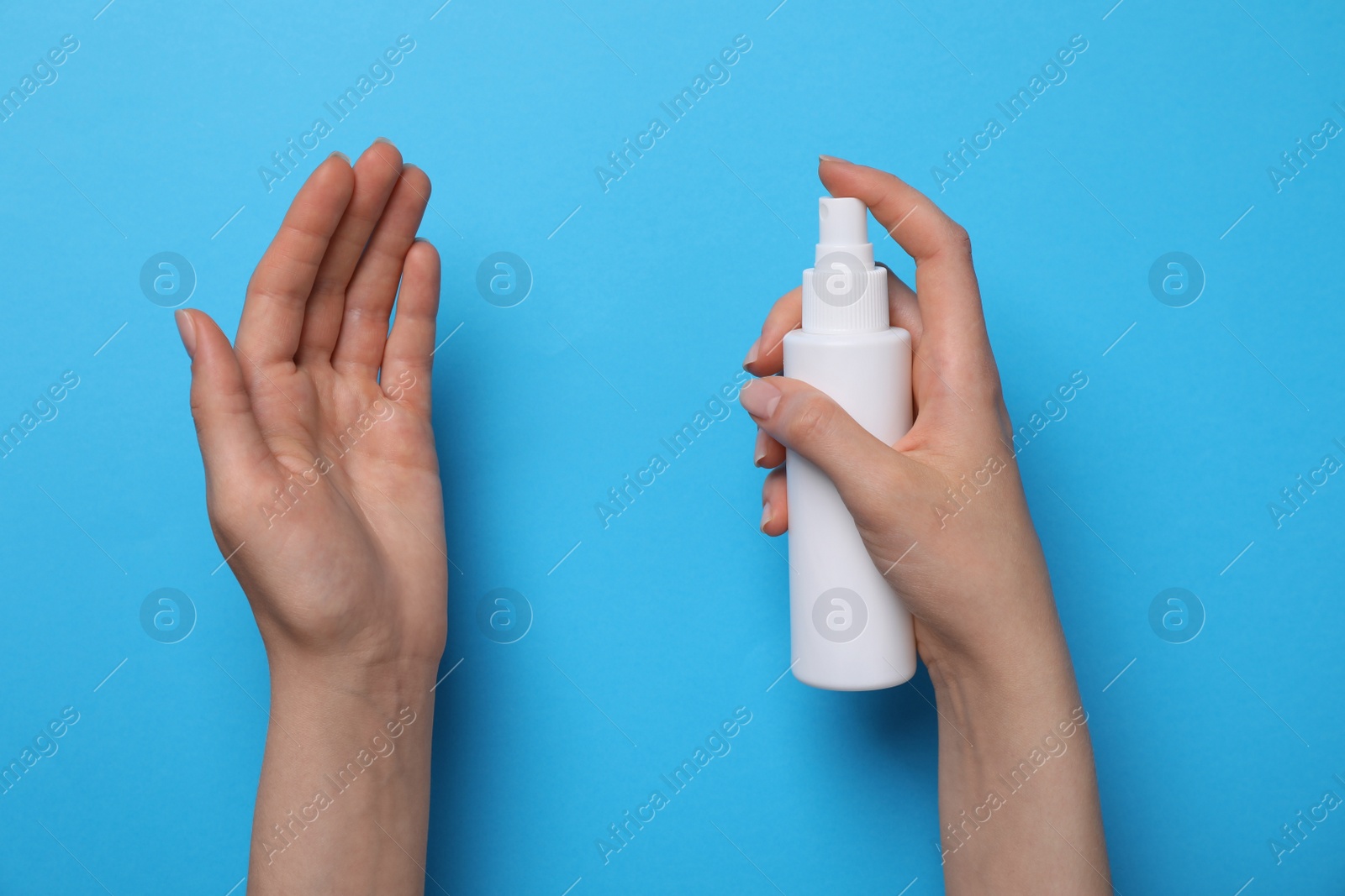 Photo of Woman spraying antiseptic onto hand on light blue background, closeup. Safety equipment