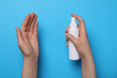 Woman spraying antiseptic onto hand on light blue background, closeup. Safety equipment