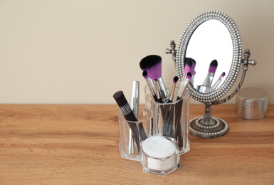 Photo of Organizer with makeup cosmetic products and mirror on table against light wall. Space for text