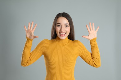 Woman in yellow turtleneck sweater showing number ten with her hands on grey background