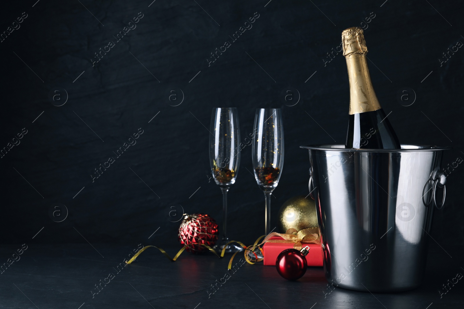 Photo of Happy New Year! Bottle of sparkling wine in bucket and glasses on black background