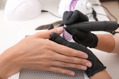 Photo of Professional manicurist working with client at white table, closeup