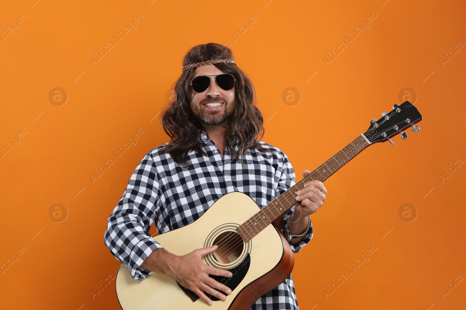 Photo of Hippie man in sunglasses playing guitar on orange background