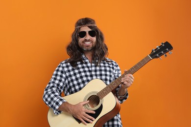 Photo of Hippie man in sunglasses playing guitar on orange background