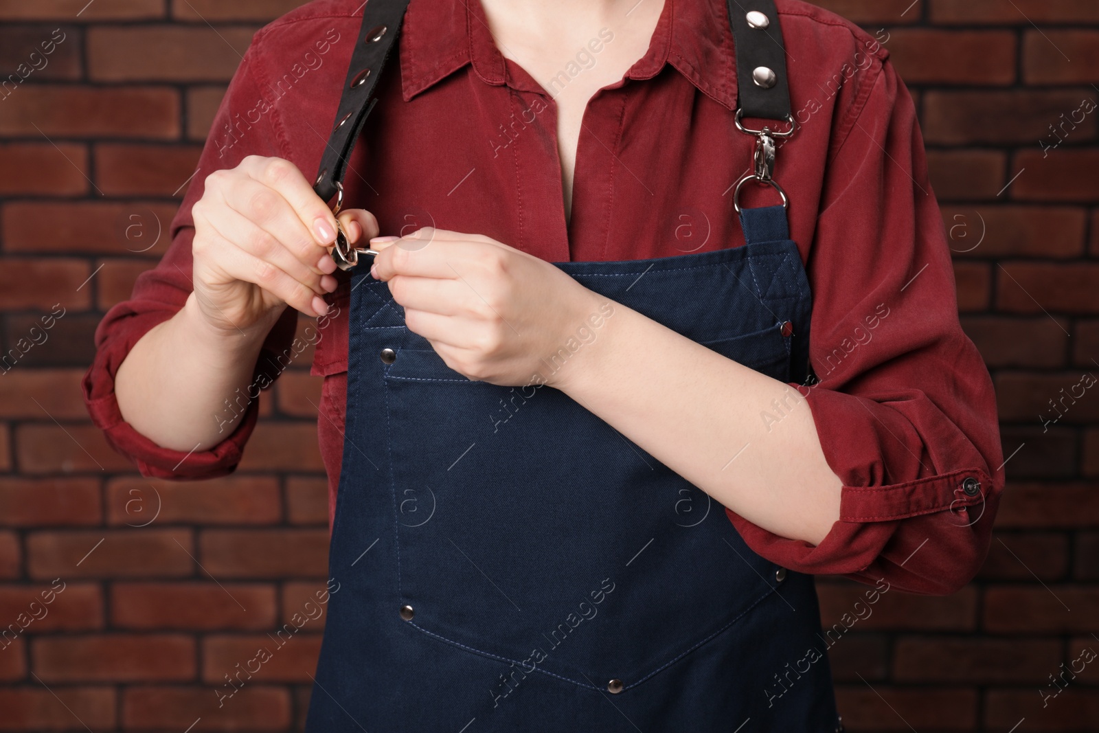 Photo of Woman putting on blue apron near red brick wall, closeup