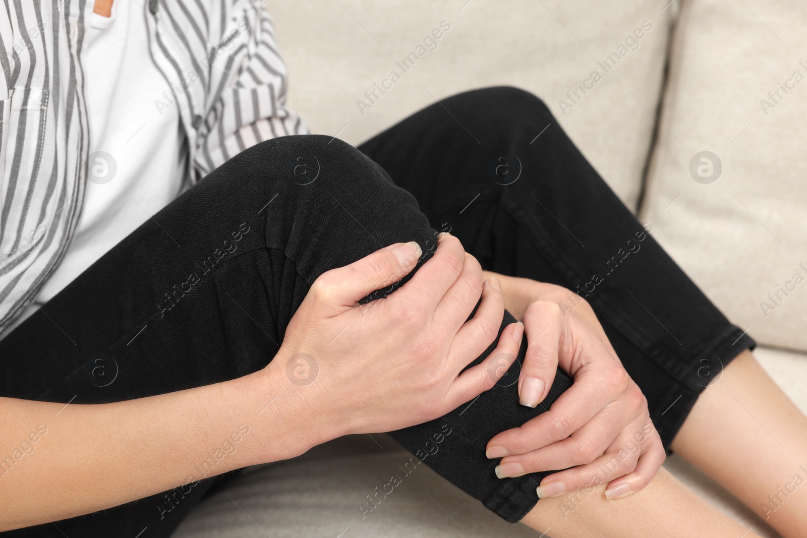 Photo of Woman suffering from knee pain on sofa indoors, closeup. Arthritis symptoms