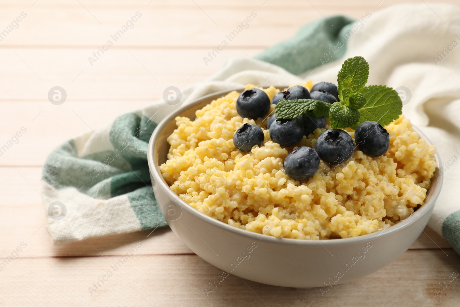 Photo of Tasty millet porridge with blueberries and mint in bowl on light wooden table, closeup. Space for text