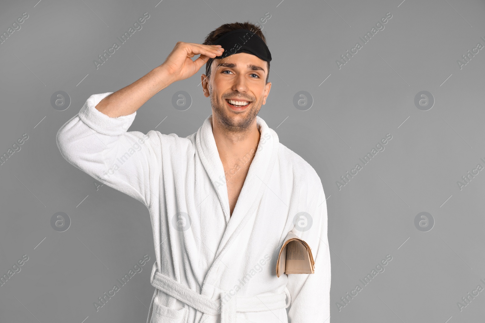 Photo of Happy young man in bathrobe with newspaper on grey background