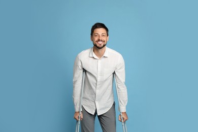 Portrait of happy man with crutches on light blue background
