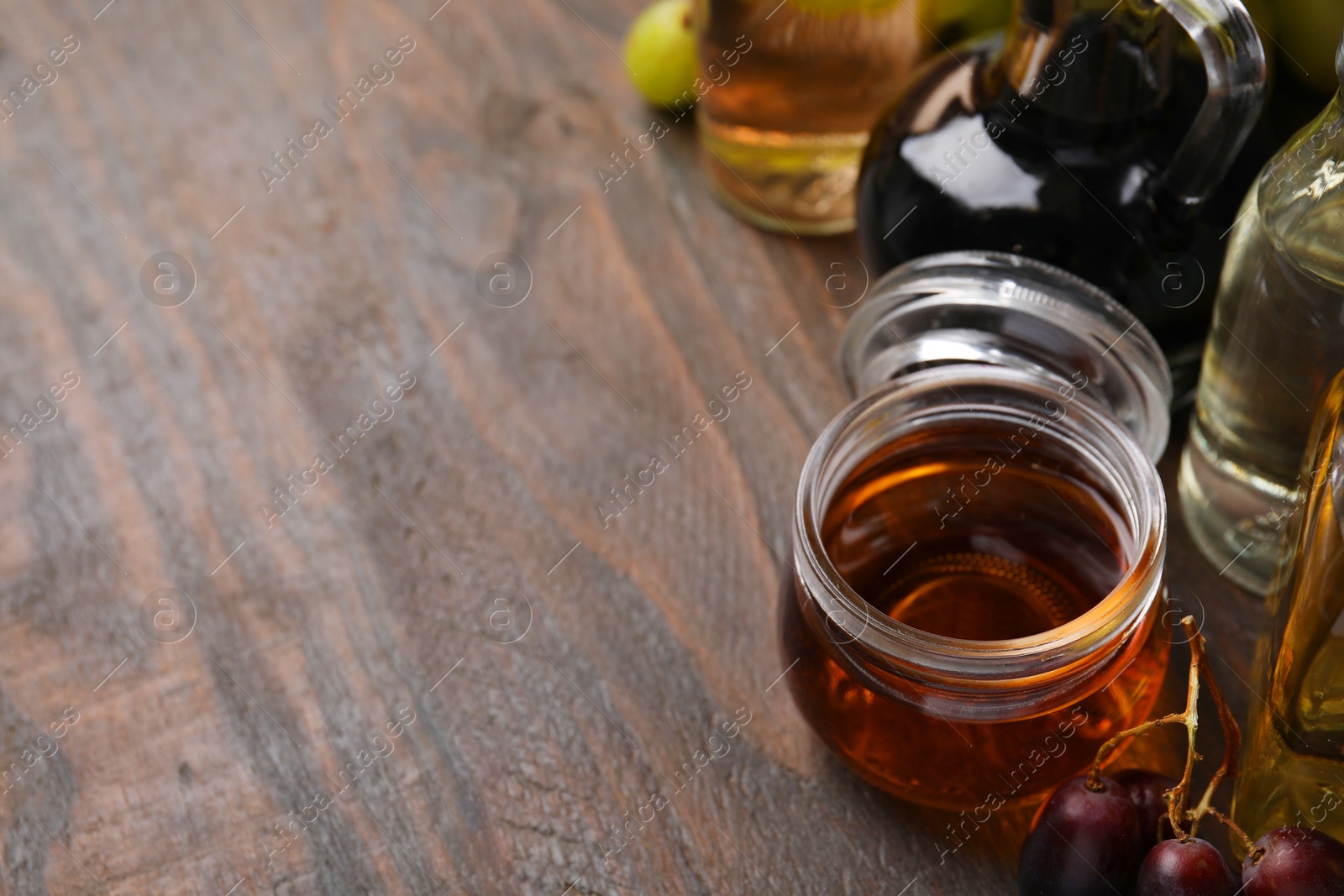 Photo of Different types of vinegar and grapes on wooden table, space for text