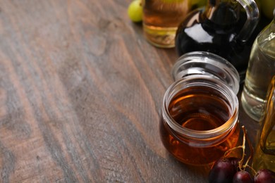 Photo of Different types of vinegar and grapes on wooden table, space for text