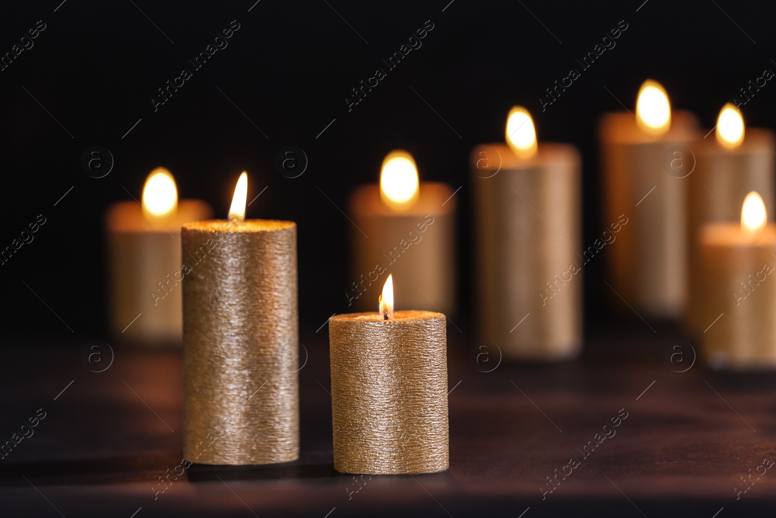 Photo of Burning gold candles on table against black background, space for text