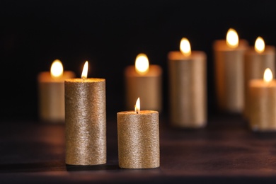 Photo of Burning gold candles on table against black background, space for text