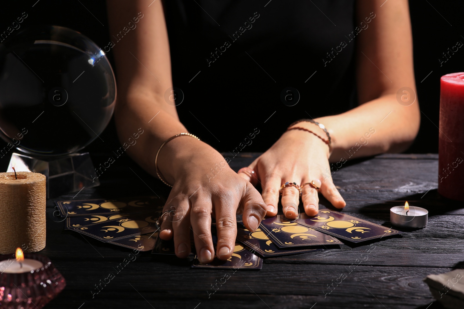 Photo of Soothsayer predicting future with tarot cards at table in darkness, closeup