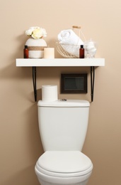 Shelf with different stuff on beige wall above toilet bowl in restroom interior