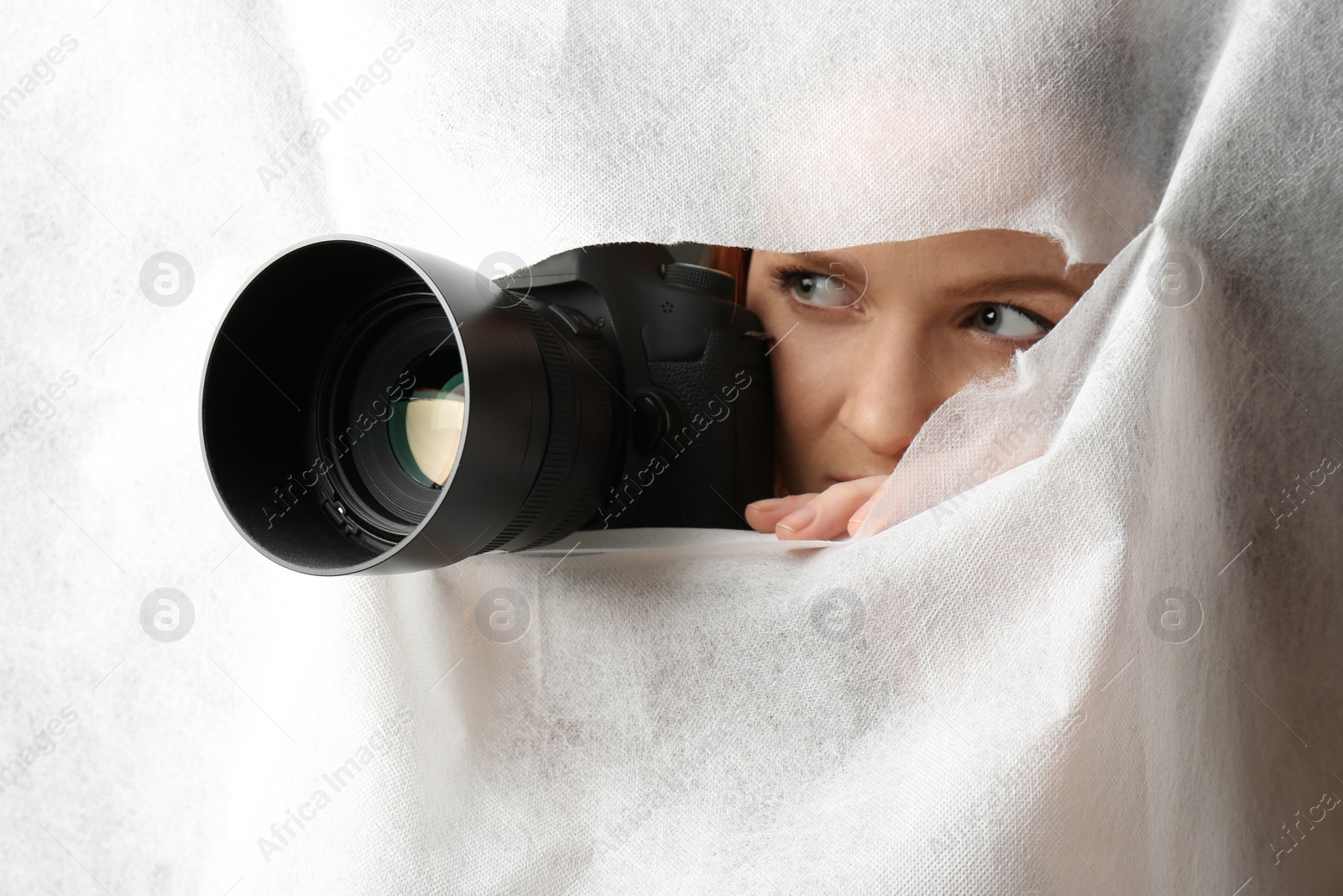 Photo of Hidden woman with camera spying through hole in white fabric