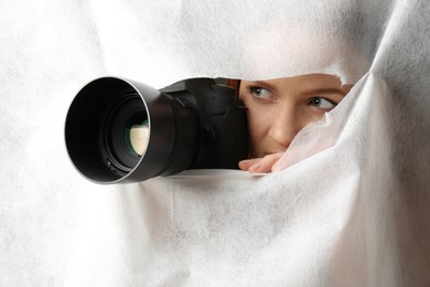 Photo of Hidden woman with camera spying through hole in white fabric
