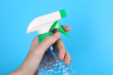 Photo of Woman holding plastic spray bottle on light blue background, closeup