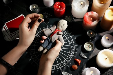 Photo of Woman stabbing voodoo doll with needle at table, closeup. Curse ceremony