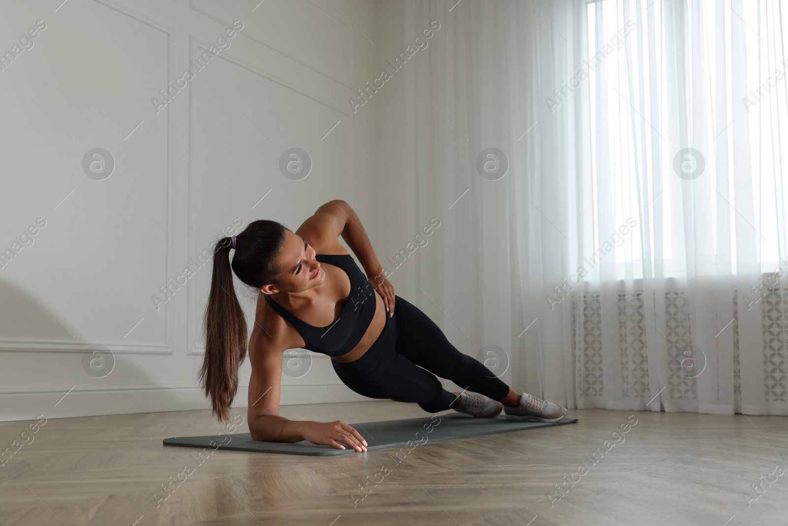 Photo of Young woman doing side plank exercise at home