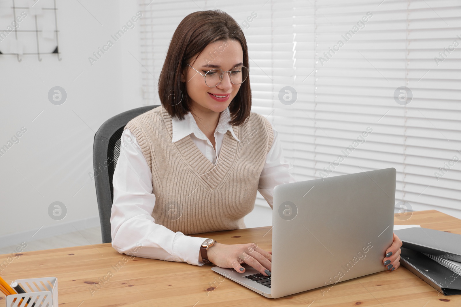 Photo of Happy young intern working with laptop at table in modern office