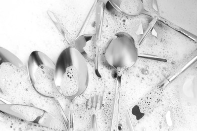 Photo of Washing silver spoons, forks and knives in foam, above view