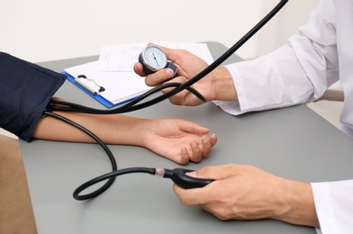 Doctor checking patient's blood pressure at table in office, closeup