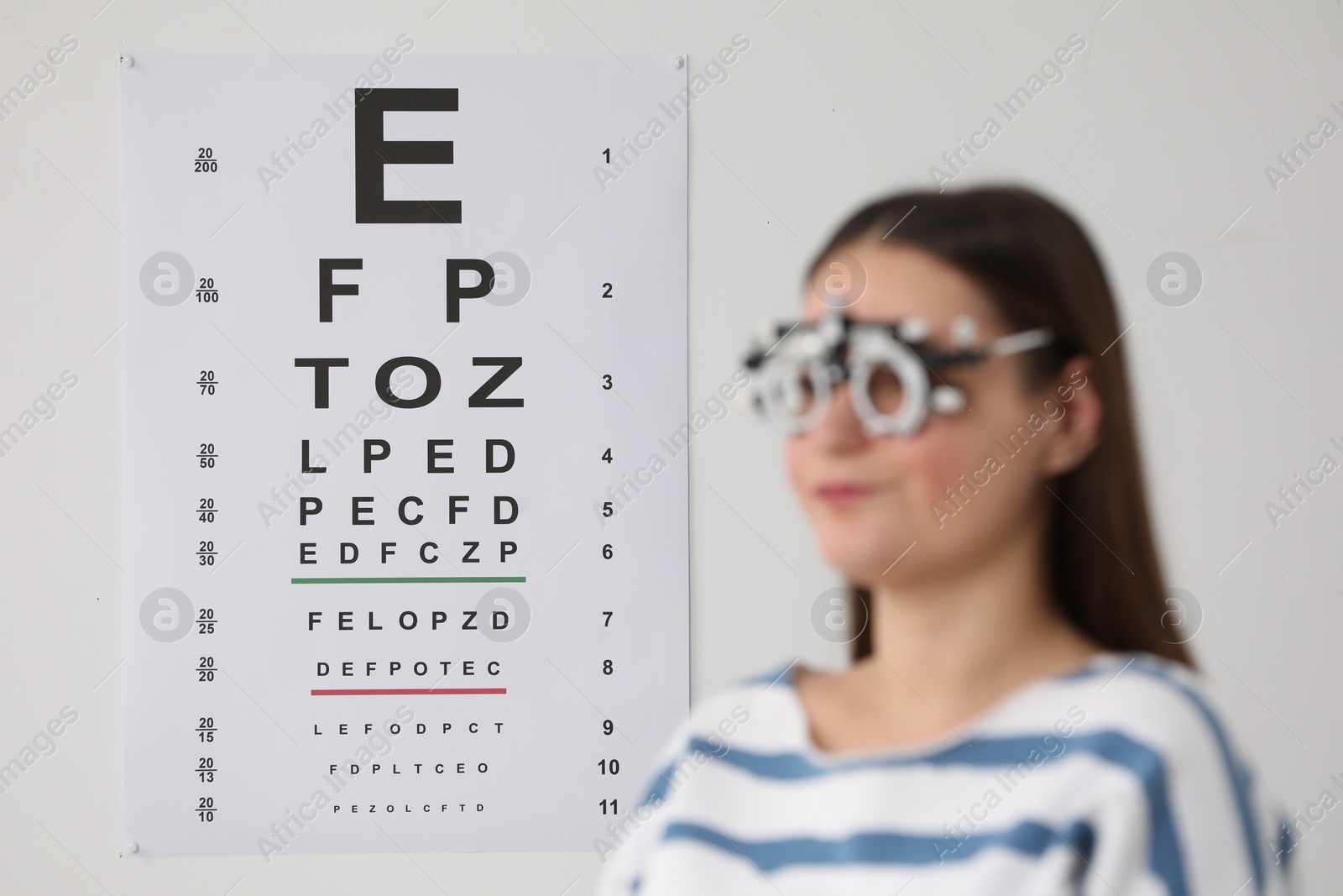 Photo of Young woman with trial frame against vision test chart, selective focus