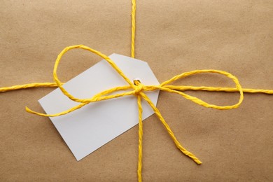 Photo of Parcel wrapped in kraft paper with tag as background, closeup